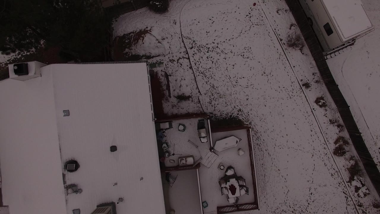 Overhead snowy house roof beside a yard and driveway.