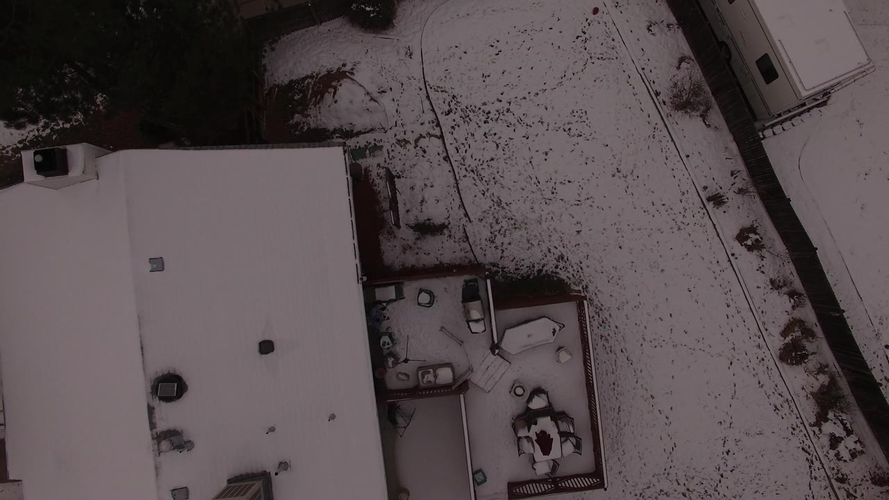 Aerial frame over Jefferson County, Colorado, with the broad white roof centered and a snowy yard and neighboring structure along the right side, with no visible people.