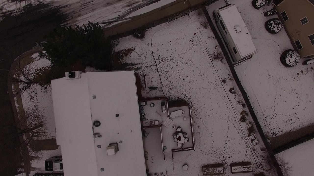 Nearly vertical aerial frame in Jefferson County, Colorado with a large snow-covered roof, adjoining yard, dark residential street, and no visible people.