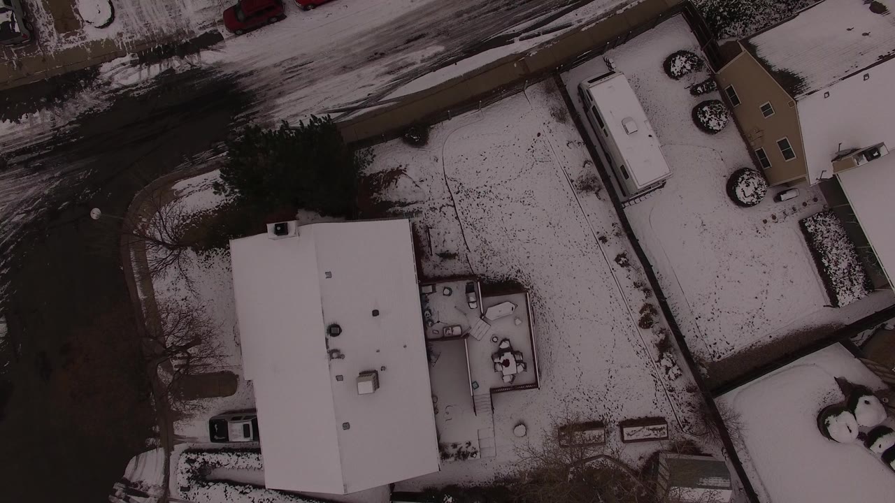 Overhead winter view of snow-covered residential roofs and a dark road.