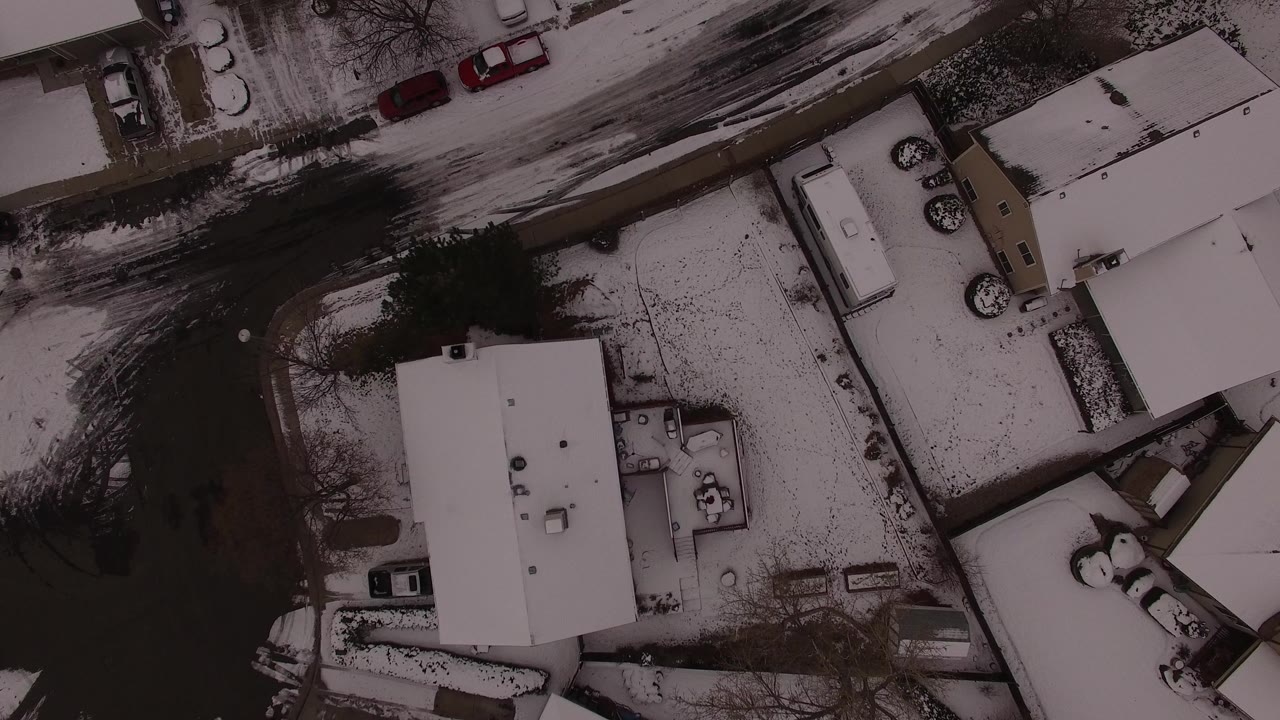 Top-down snowy neighborhood with houses, dark streets, and parked cars.