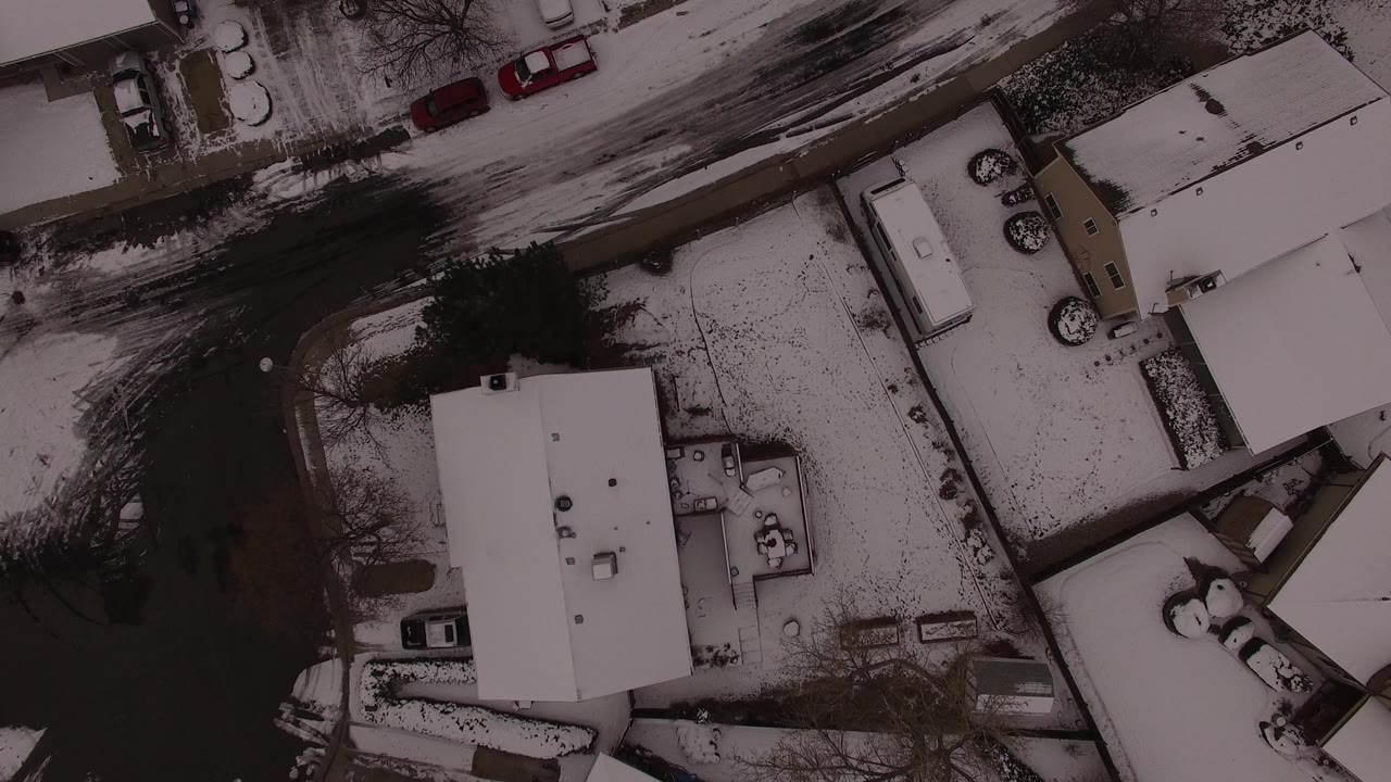 Aerial frame over Jefferson County, Colorado homes, showing pale roofs, a curved dark road, snow-dusted yards, and no visible people.