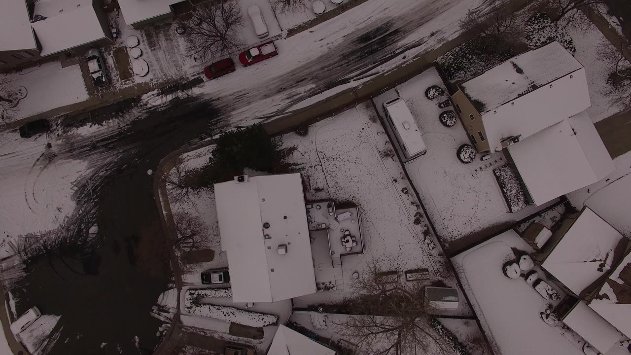 Overhead view of snowy homes and parked cars along dark residential streets.