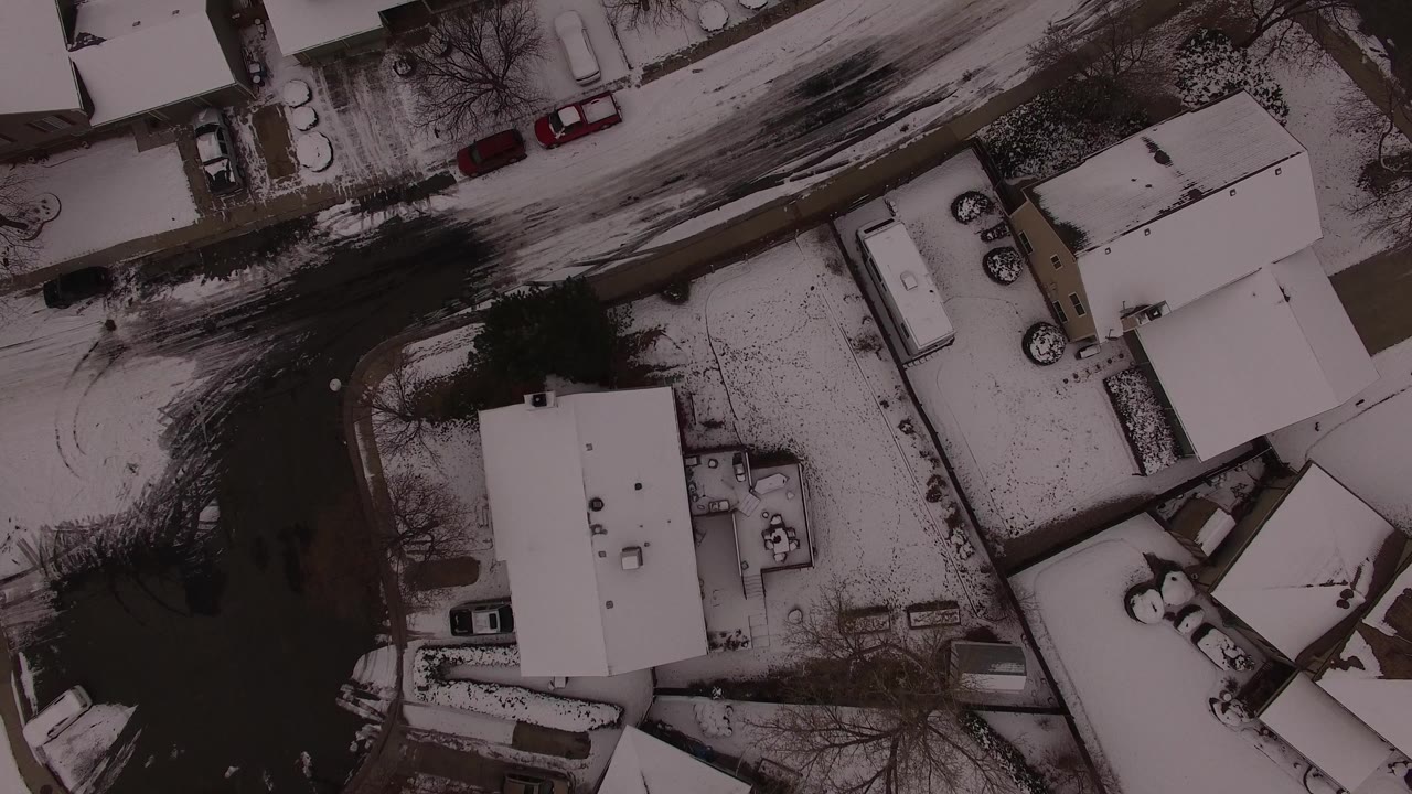 Top-down Jefferson, Colorado view with a central snow-covered roof, parked cars near driveways, a dark road curve, bare trees, and no clearly visible people.