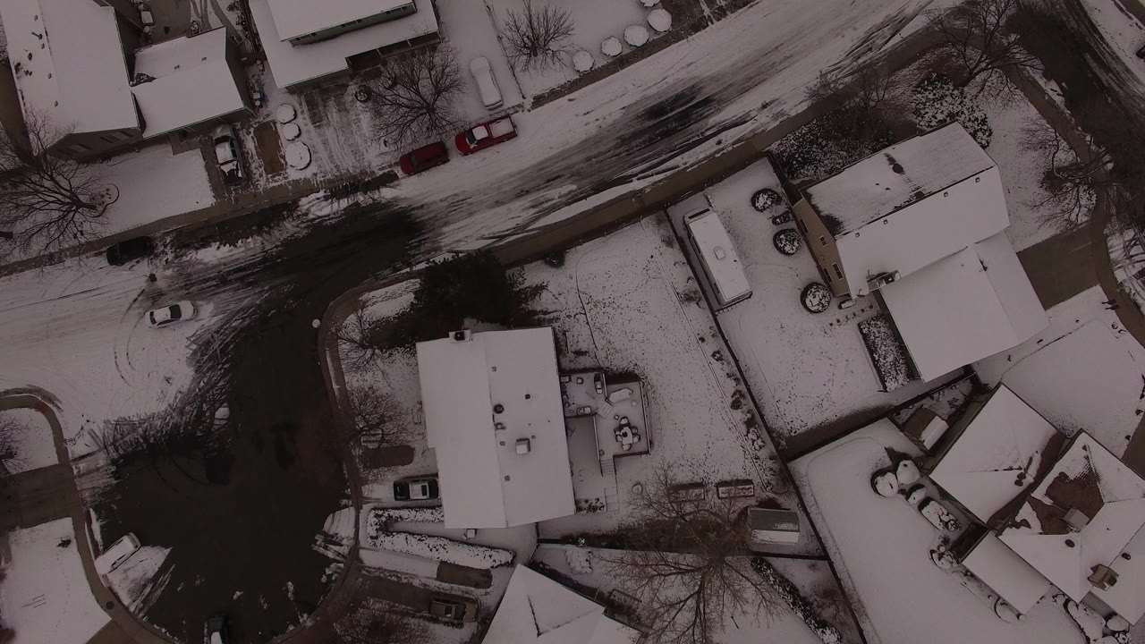 Overhead aerial view in Jefferson County, Colorado showing snow-covered homes, bare trees, parked cars, and a dark residential street with no visible people.