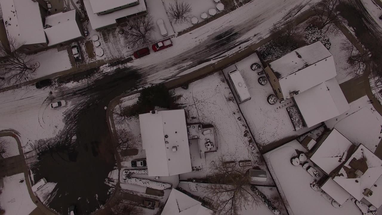 Aerial winter frame over Jefferson County, Colorado with white roofs, dark pavement, driveways, and several vehicles visible at neighborhood scale.