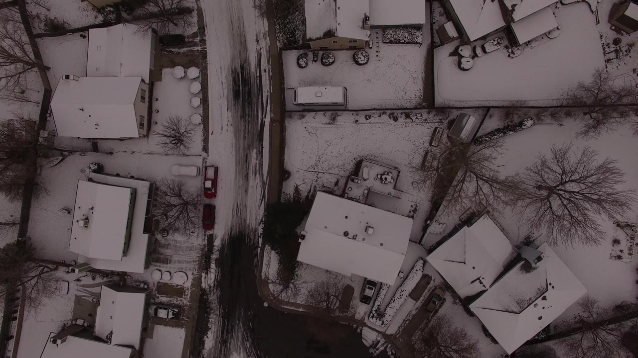 Top-down aerial view over Jefferson County, Colorado houses, snow-covered roofs, bare trees, parked cars, and dark residential streets with no visible people.