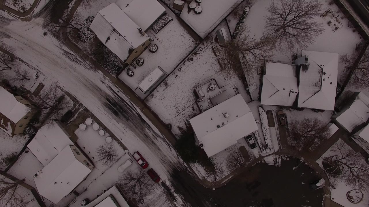 Overhead monochrome view of snowy houses and a plowed street.