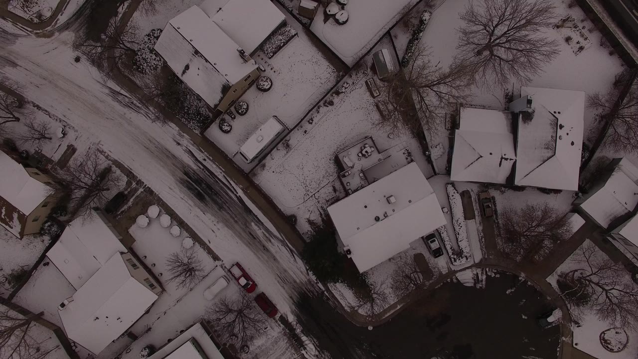 Overhead Jefferson County, Colorado view with a diagonal plowed road, snow-covered houses, dark driveways, leafless trees, and no visible people.