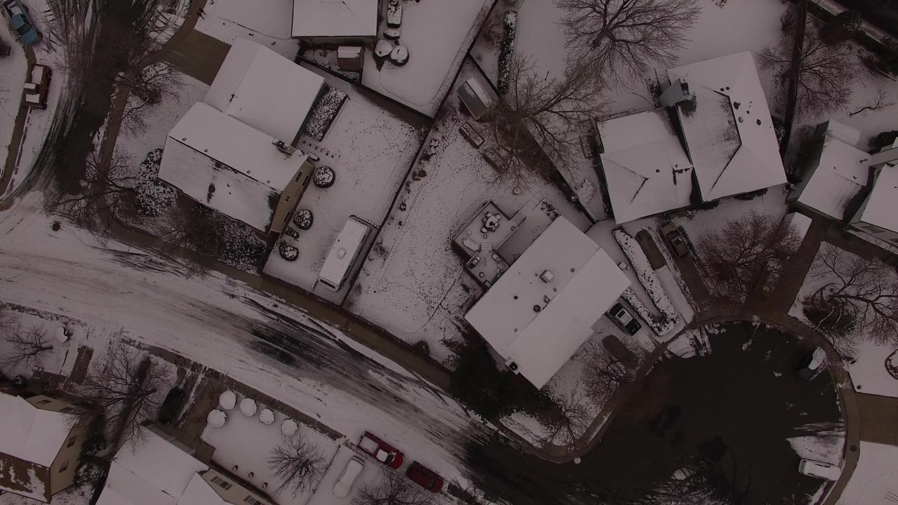 The next overhead frame in Jefferson County, Colorado keeps the snowy houses centered, with dark pavement cutting across the lower half and no visible people.