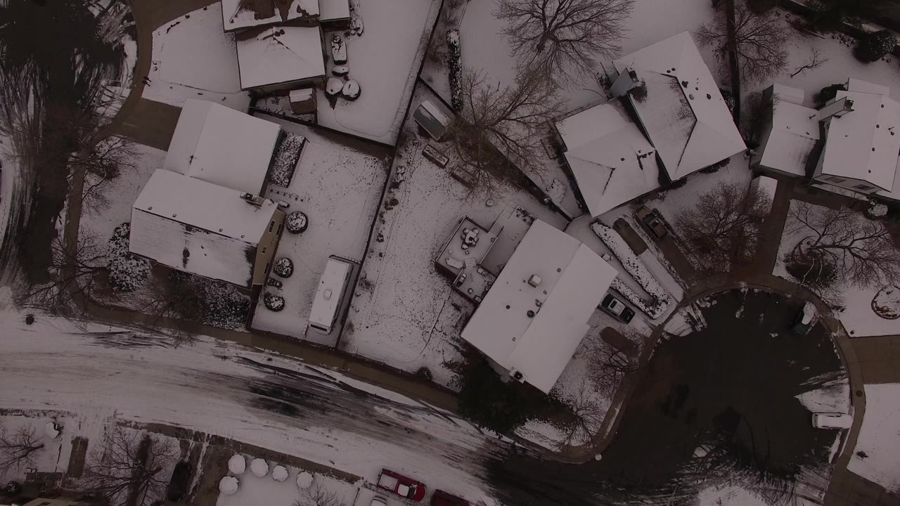 Top-down view of Jefferson County, Colorado houses around a curved winter road, with white roofs, dark pavement, bare trees, and no visible people.
