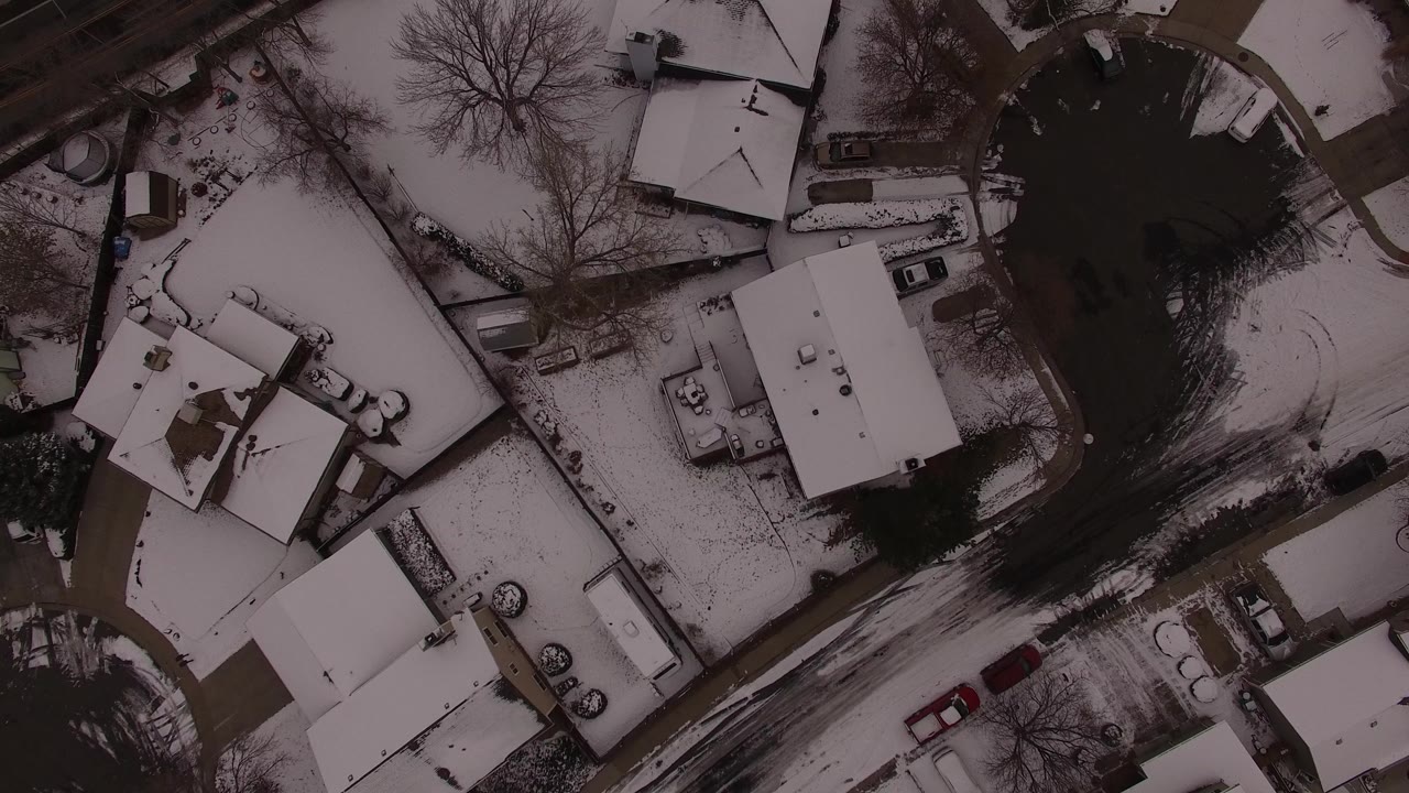 Overhead aerial frame in Jefferson, Colorado showing snow-covered roofs, bare trees, driveways, and a curving residential road with no visible people.