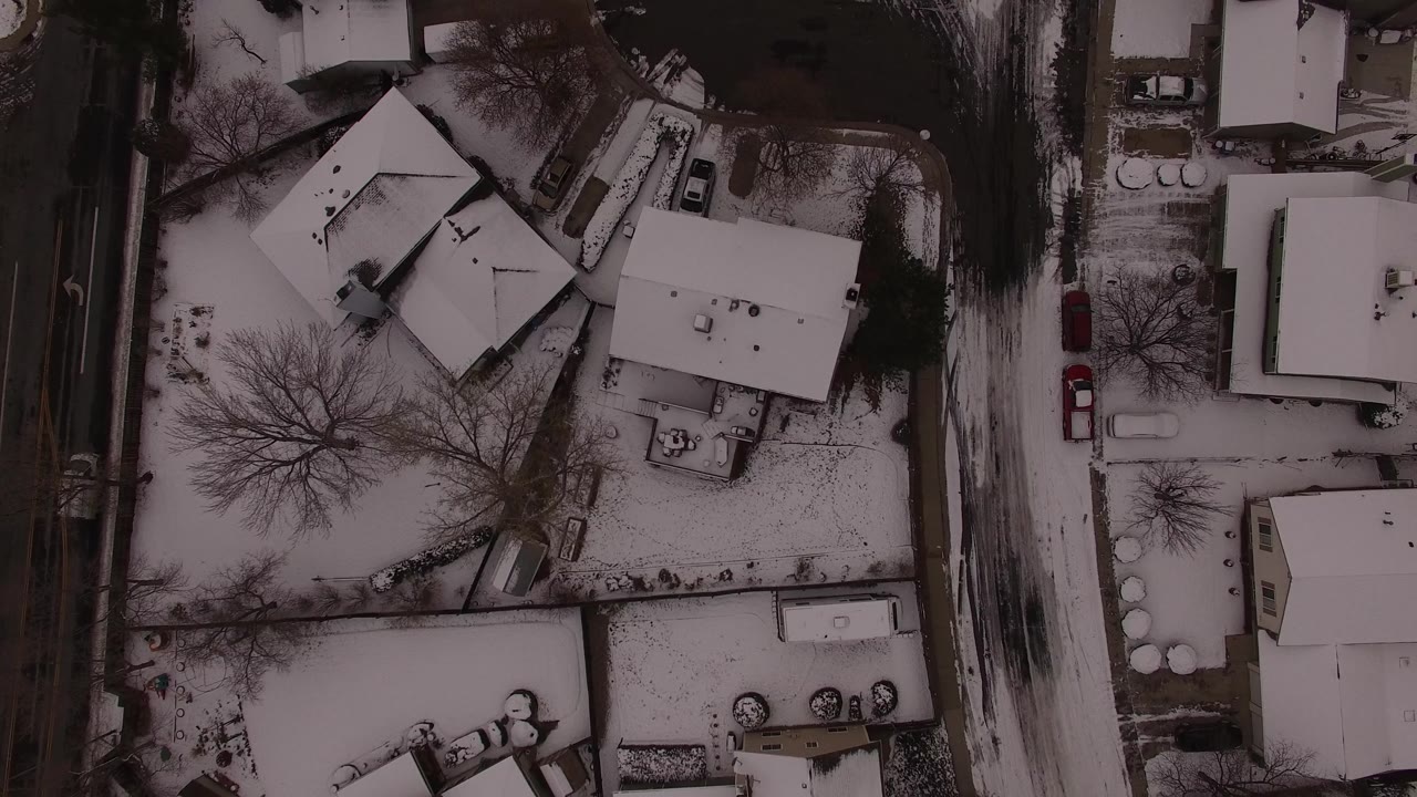 Top-down frame showing snowy residential roofs, fenced yards, leafless trees, and a road along the right side in Jefferson County, Colorado, with no visible people.
