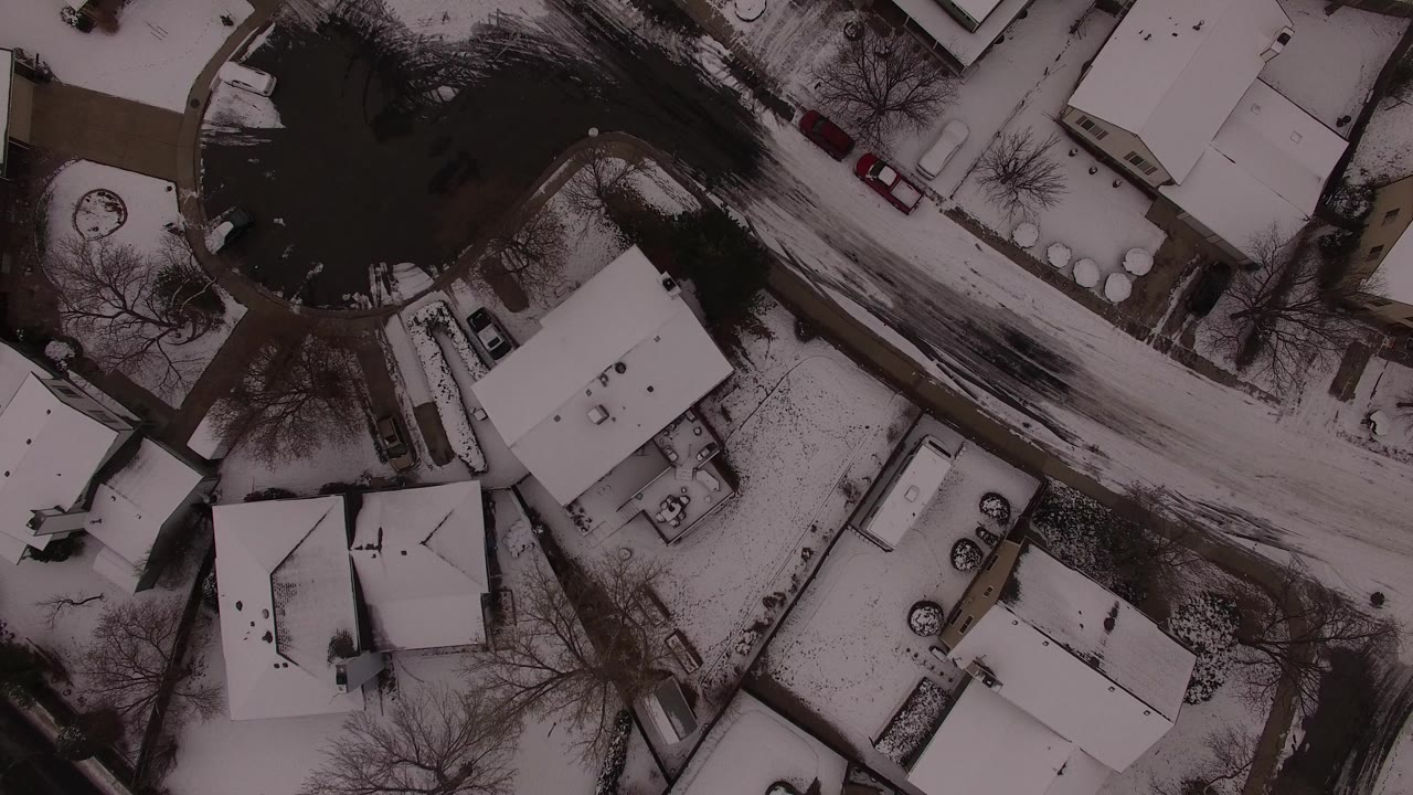 Top-down aerial frame over Jefferson County, Colorado homes, showing snow-covered roofs, driveways, leafless trees, parked cars, and no visible people.