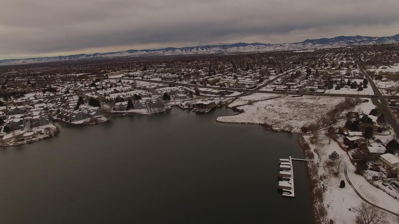 Aerial frame over Jefferson County, Colorado, with boat docks at the lower edge, snow on lakeside yards, residential streets beyond, and no visible people.