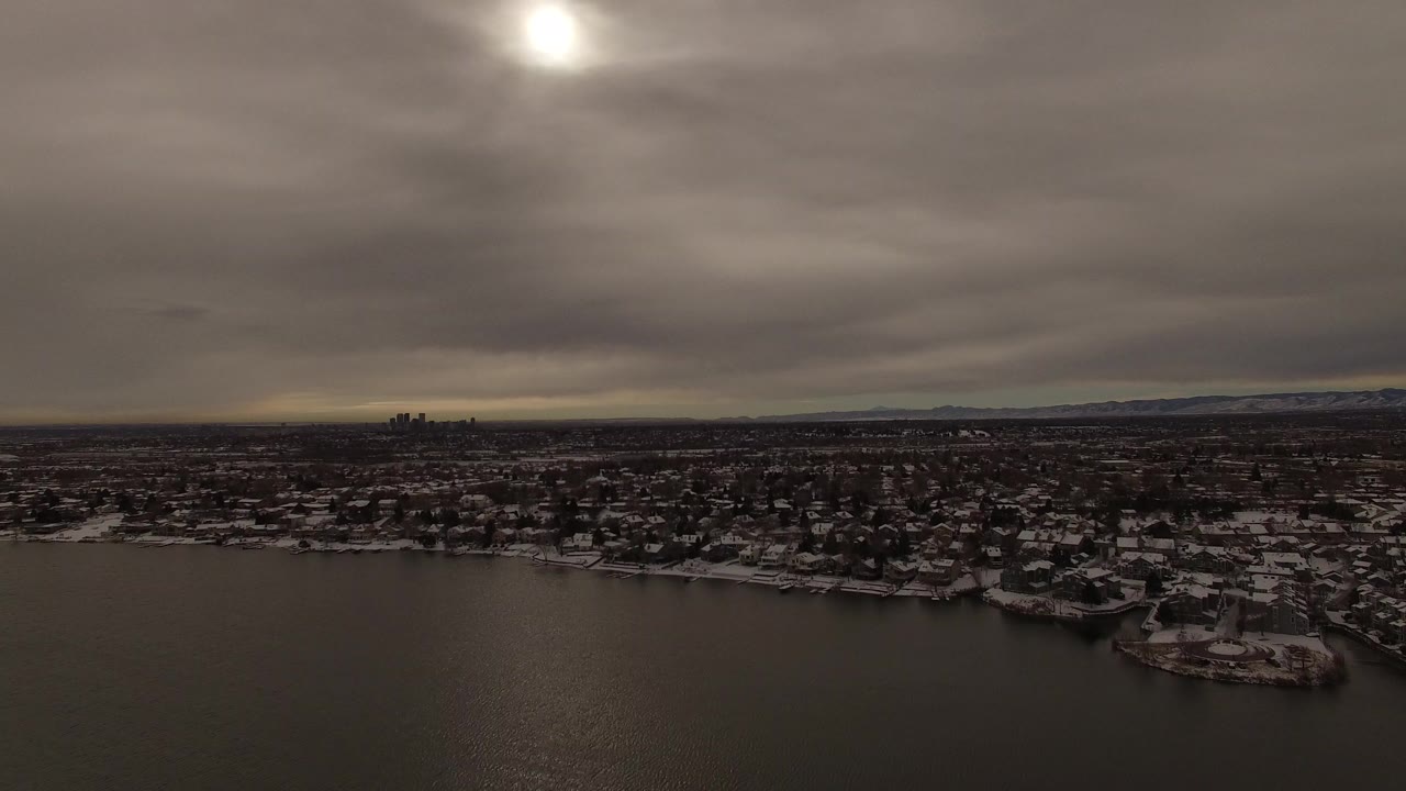 Wide aerial view of snowy shoreline town under heavy clouds.