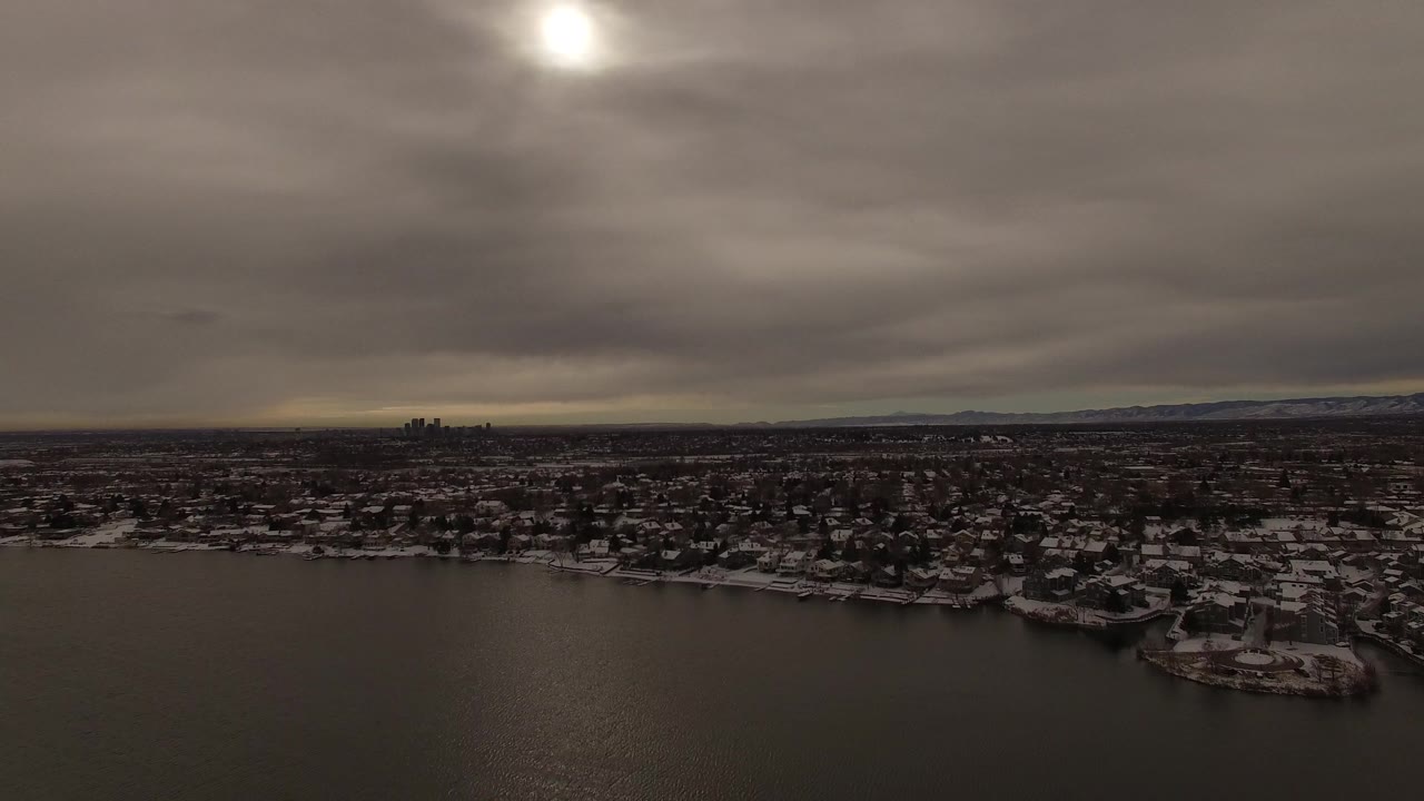 Aerial view in Jefferson County, Colorado showing a broad band of dark water, snow-dusted residential blocks, a low horizon, distant city towers, and no visible people.