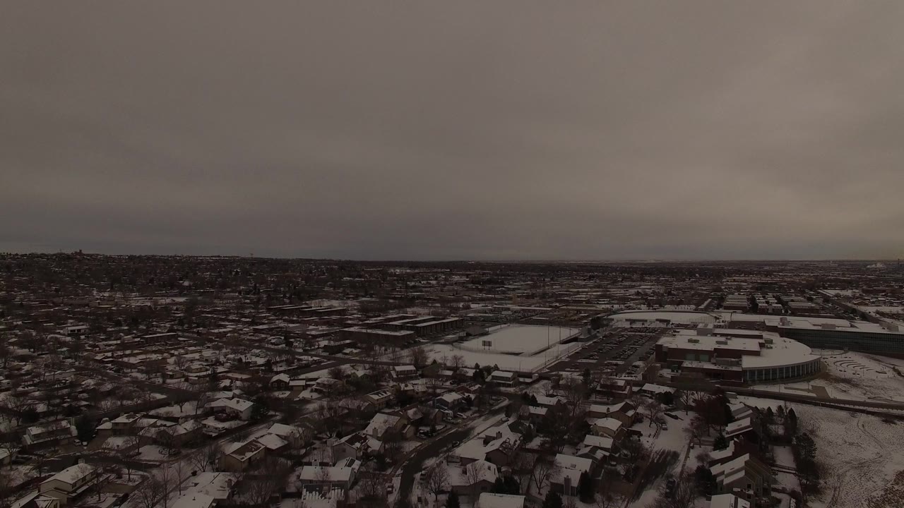 Wide overhead frame in Jefferson County, Colorado with rows of snow-covered houses, dark roads, a cluster of larger buildings, and no visible people.