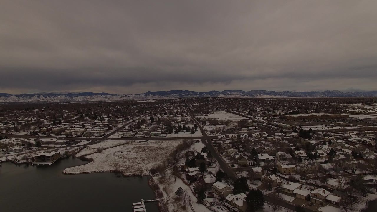 Wide aerial view of snowy lakeside neighborhoods under gray clouds