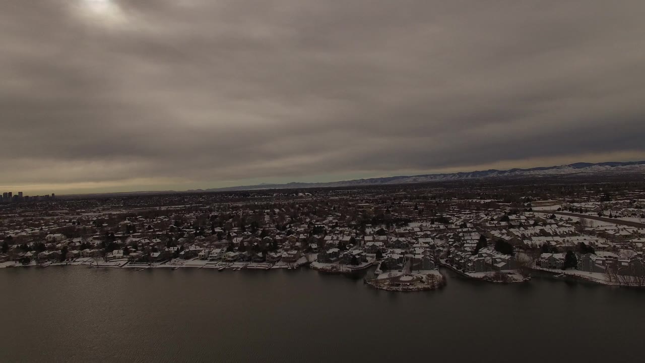 Wide drone-like view of lake, snowy homes, and distant hills.