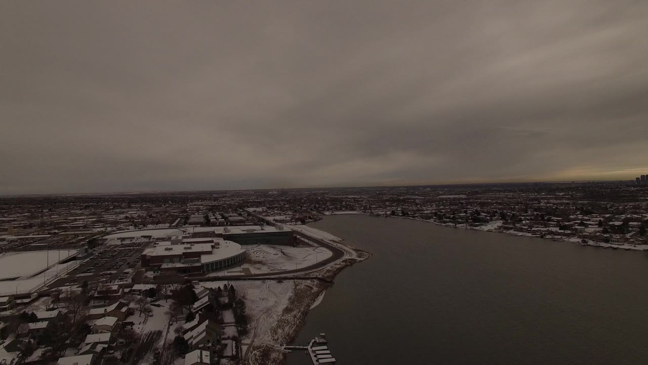 Snowy shoreline beside dark water under a heavy evening sky