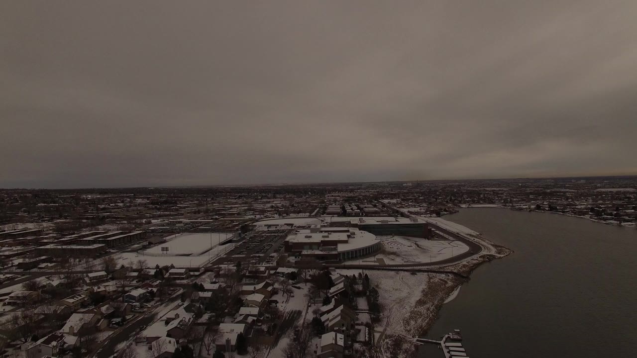 Aerial view of a dark lake beside snow-dusted homes under heavy clouds
