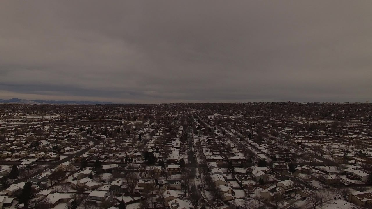 Wide aerial view of snow-covered suburban homes under a gray sky.