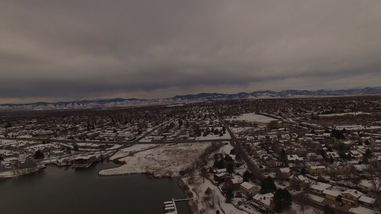 Jefferson County, Colorado aerial frame with snow-dusted homes, a lake edge, gridded roads, a low mountain horizon, and no visible people.