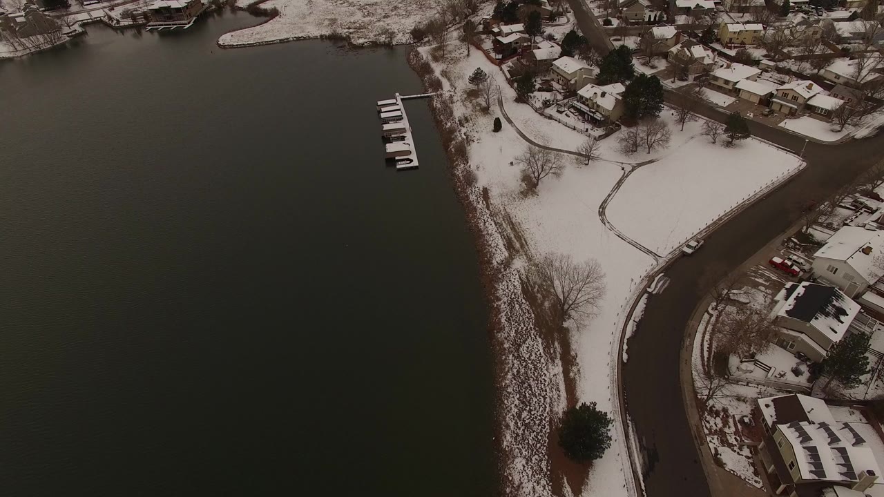 Overhead view of dark water beside snow-covered homes and shoreline roads.