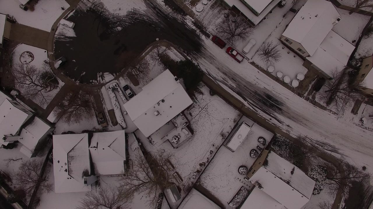 Overhead snowy residential street with houses and trees.