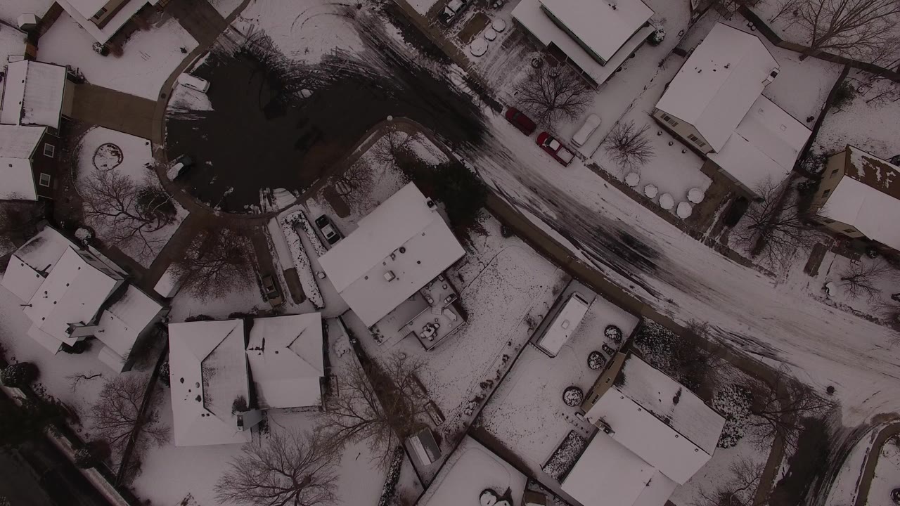 Overhead snowy suburban homes beside a dark water area and curved road.