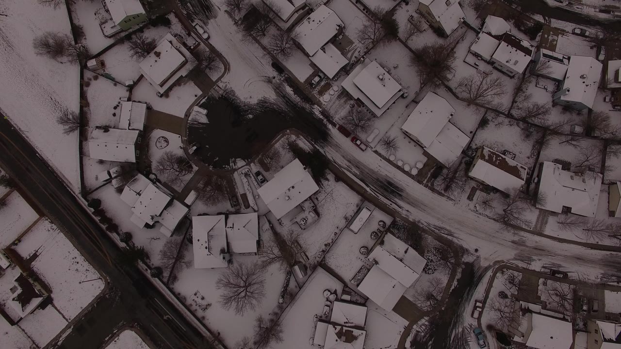 Overhead view of snow-covered houses, dark roads, bare trees, and yards in Jefferson County, Colorado, with no visible people discernible.
