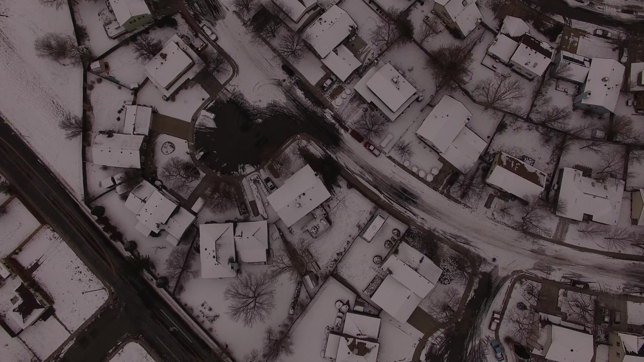 Aerial frame over Jefferson County homes showing white roofs, a curving snow-edged street, dark tree lines, and no visible people discernible.