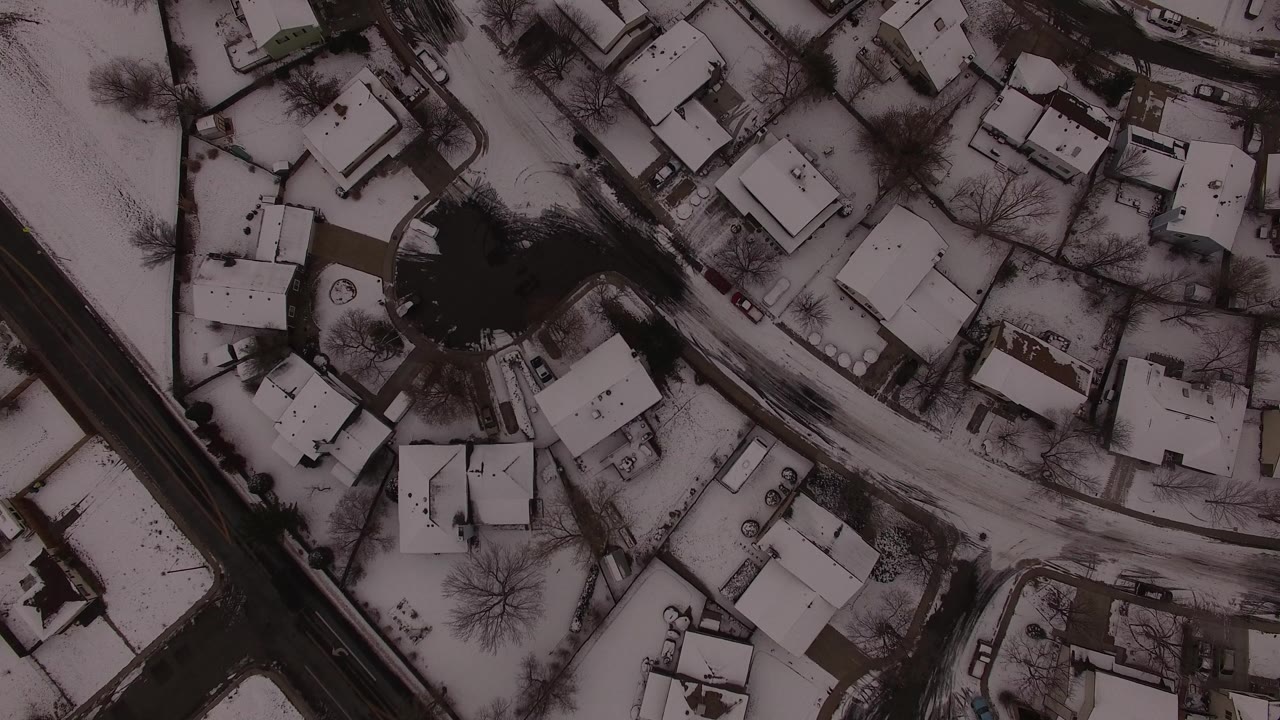 High overhead frame in Jefferson County, Colorado with snow-dusted rooftops, a winding side street, a darker road edge, and no visible people.
