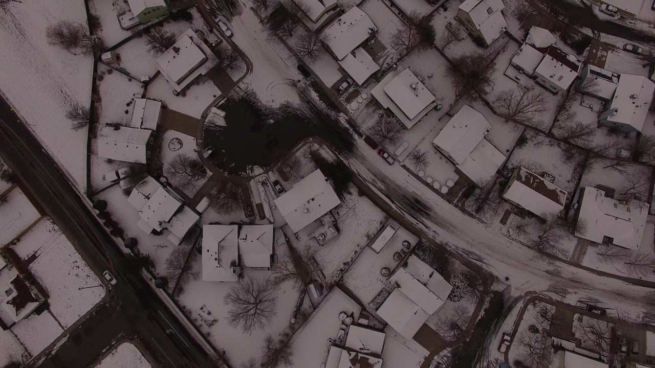 Top-down aerial view over Jefferson County, Colorado, showing snow-covered houses, curved neighborhood streets, bare trees, parked cars, and no visible people.