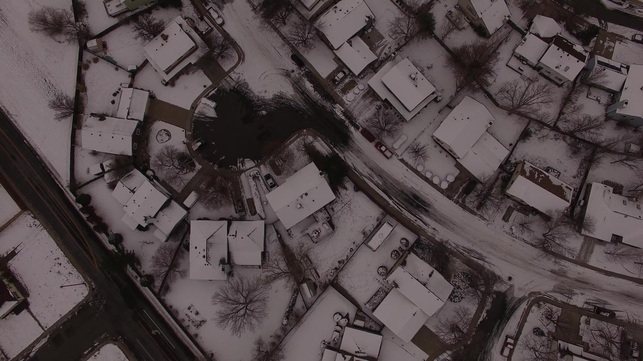 Top-down snowy neighborhood with houses, roads, bare trees, and dark water.