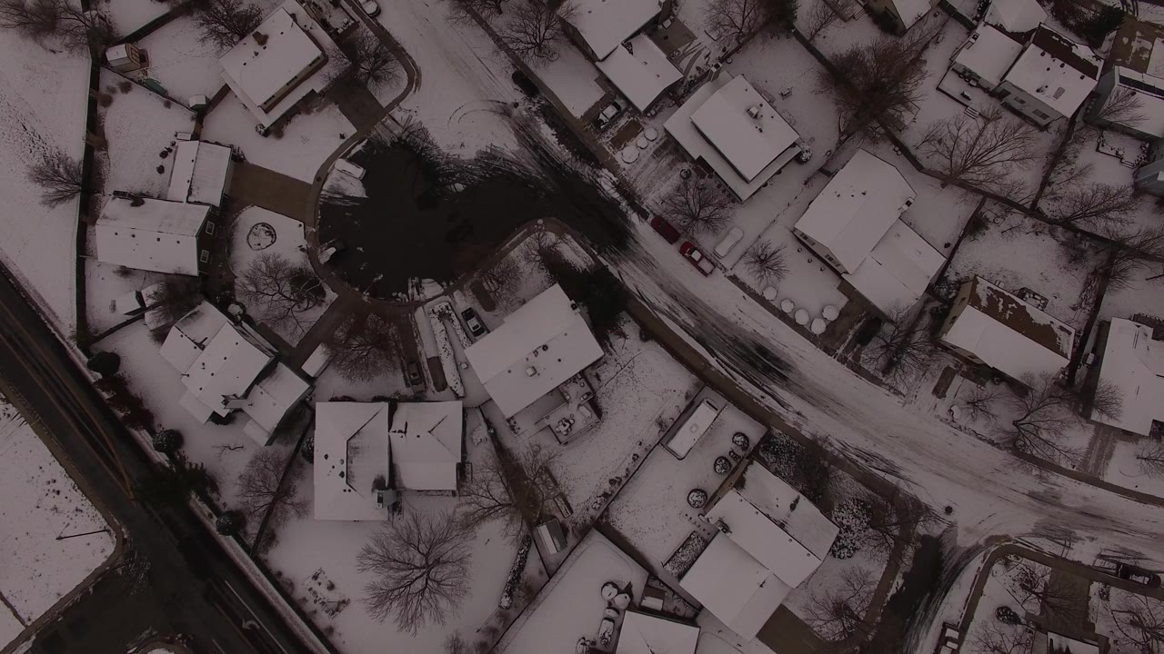 A top-down Jefferson County winter frame shows clustered houses, white roofs, dark tree canopies, parked vehicles, and no visible people along the road.