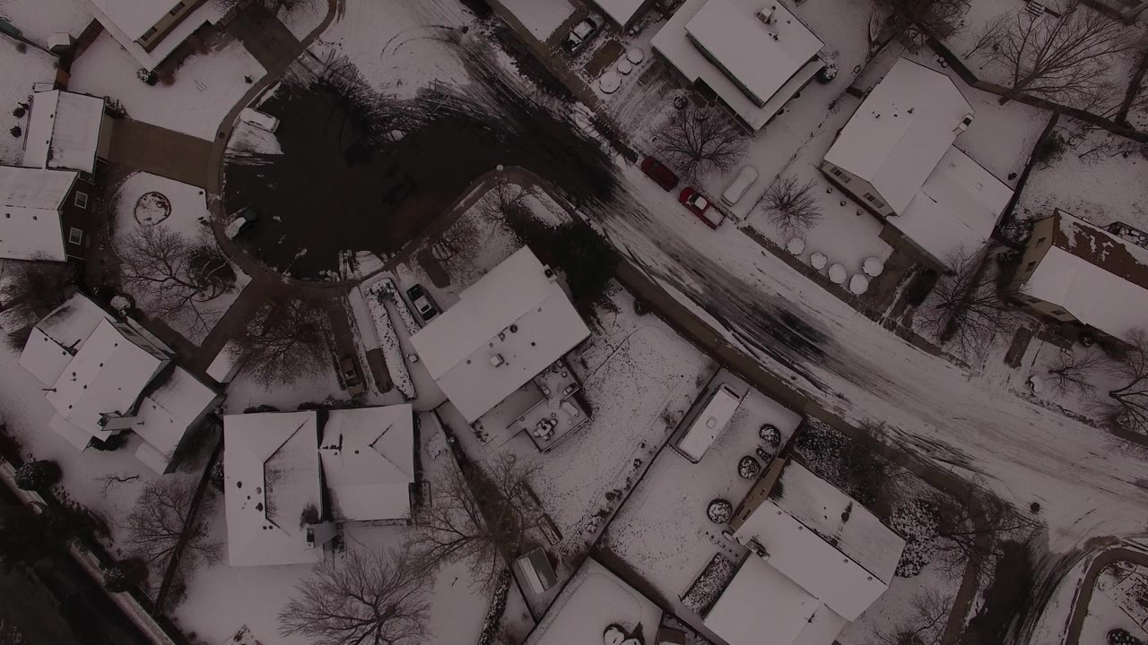 Aerial winter view of houses, parked cars, and snowy streets.
