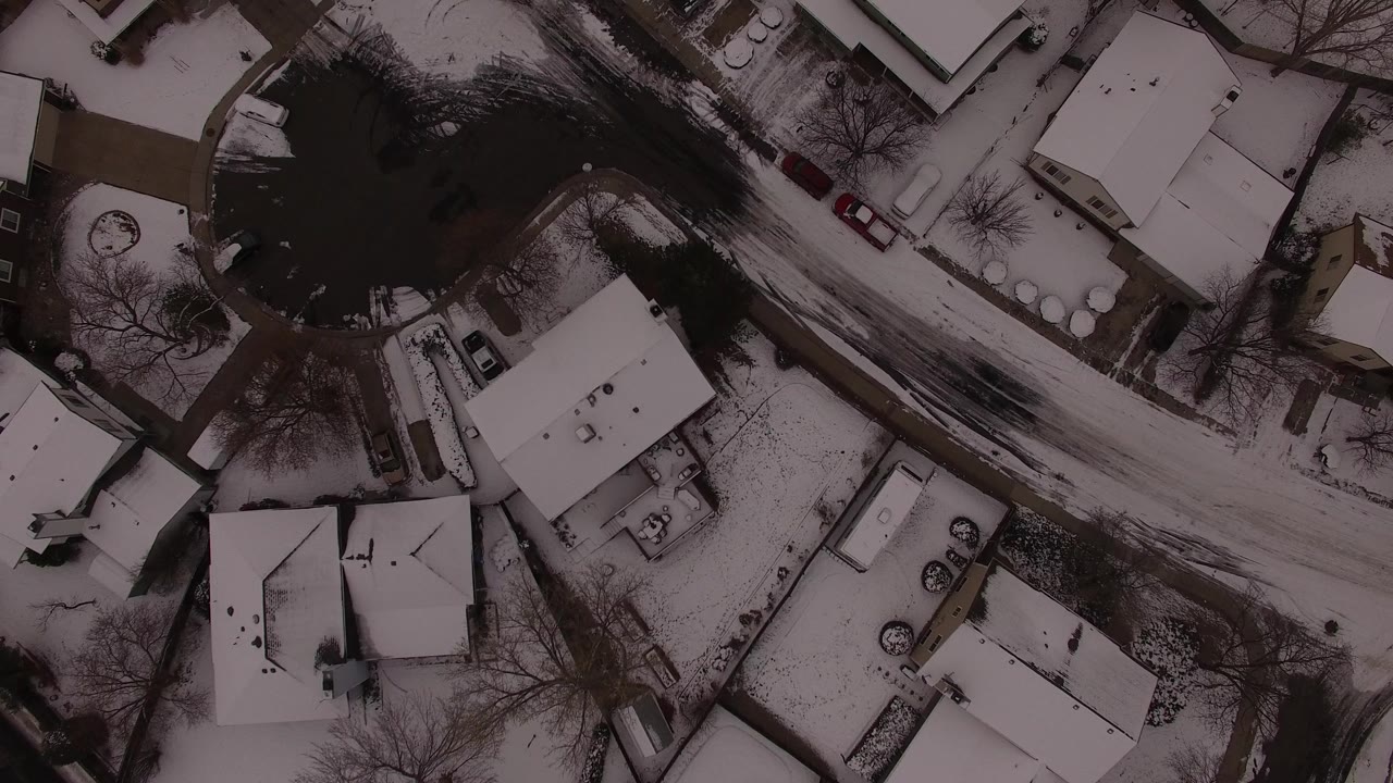 Second overhead frame in Jefferson, Colorado showing the same snowy homes, driveway edges, parked vehicles, and dark road surface around a cul-de-sac, with no visible people.