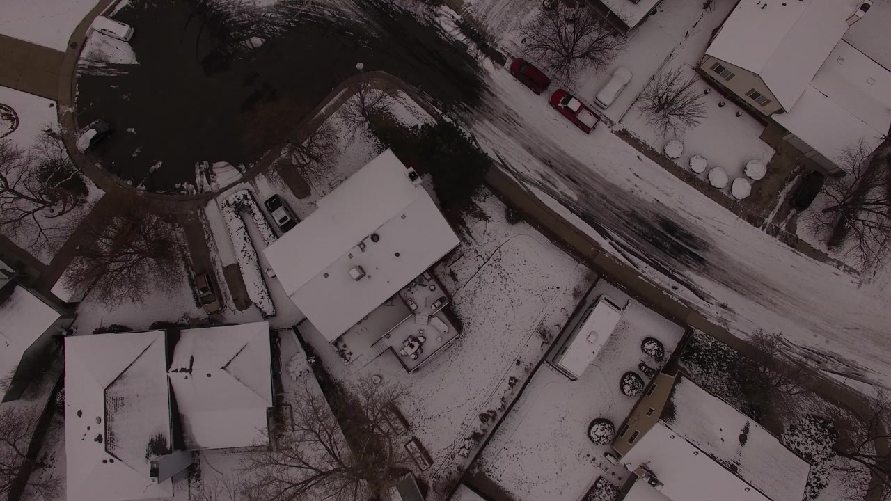 Aerial view in Jefferson County, Colorado, with white roofs, dark wet road edges, driveways, parked cars, bare trees, and no visible people.