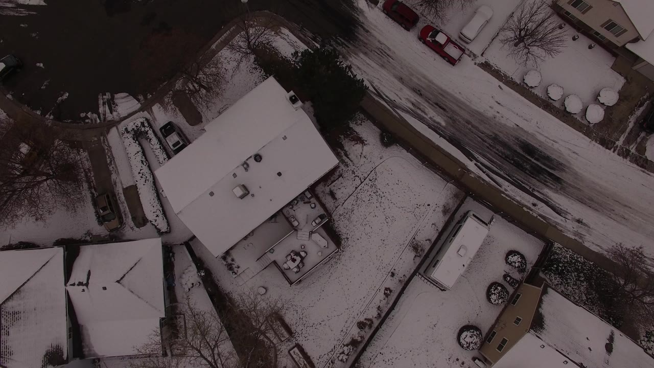 Top-down snowy residential roofs and curved street.