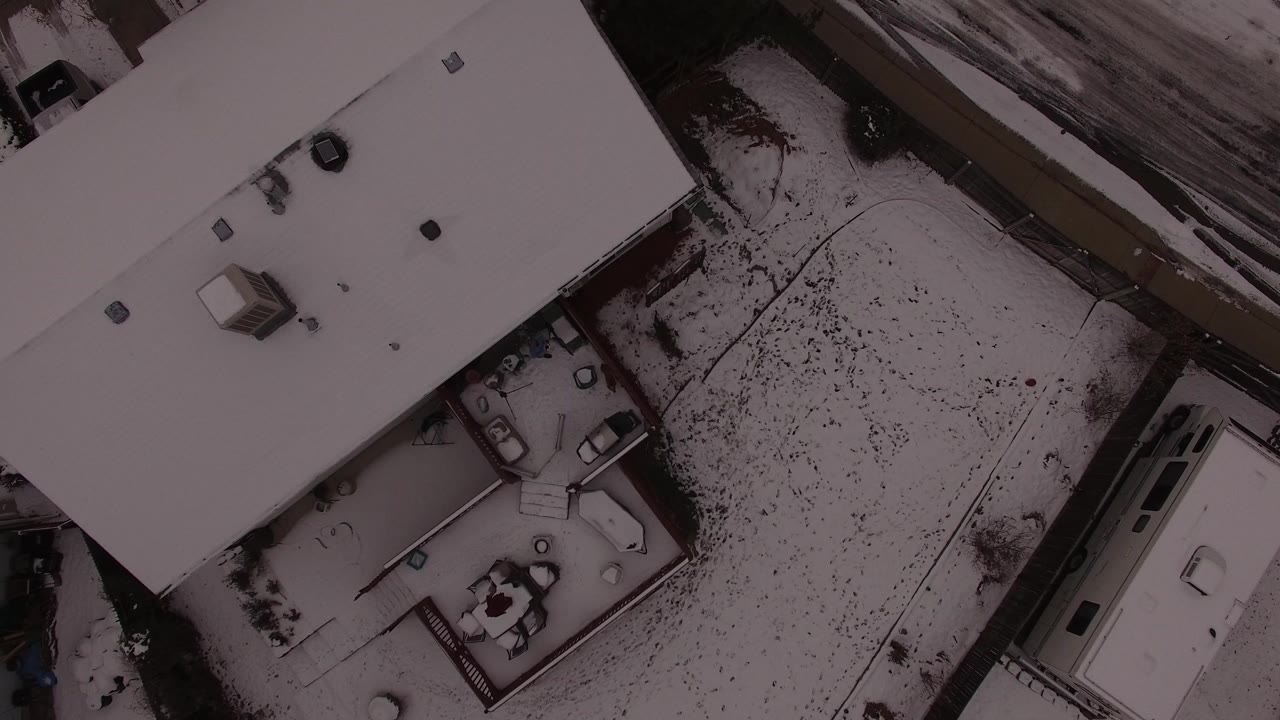 Overhead view of a snow-covered house roof and yard beside a road.