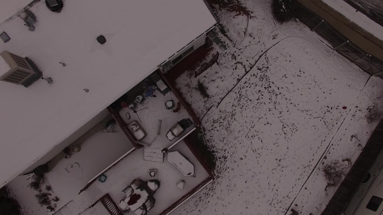 Top-down view of a snowy backyard and adjacent residential buildings.