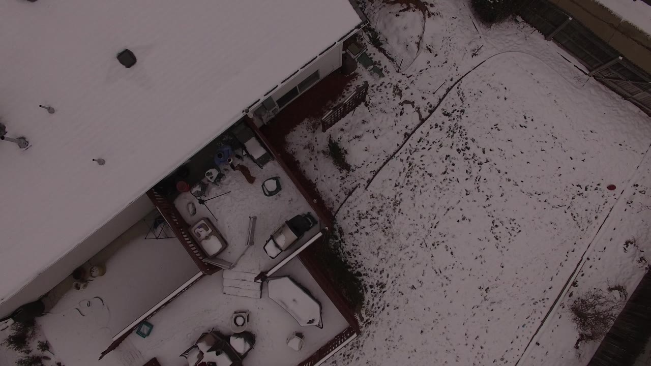 Aerial frame in Jefferson County, Colorado with rooflines and a deck along the left edge, a broad snow-covered yard to the right, and no visible people.