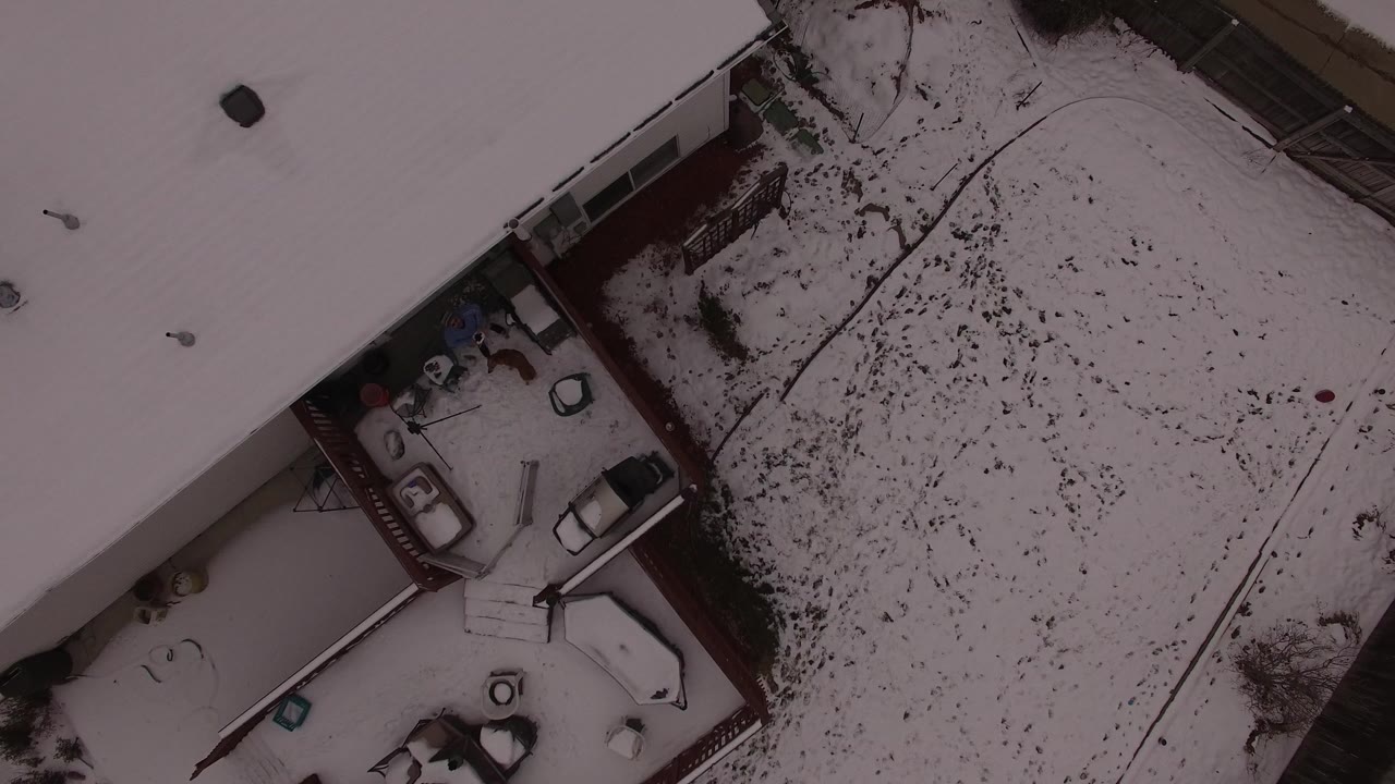 Top-down snowy residential yard with roofs and patio items.