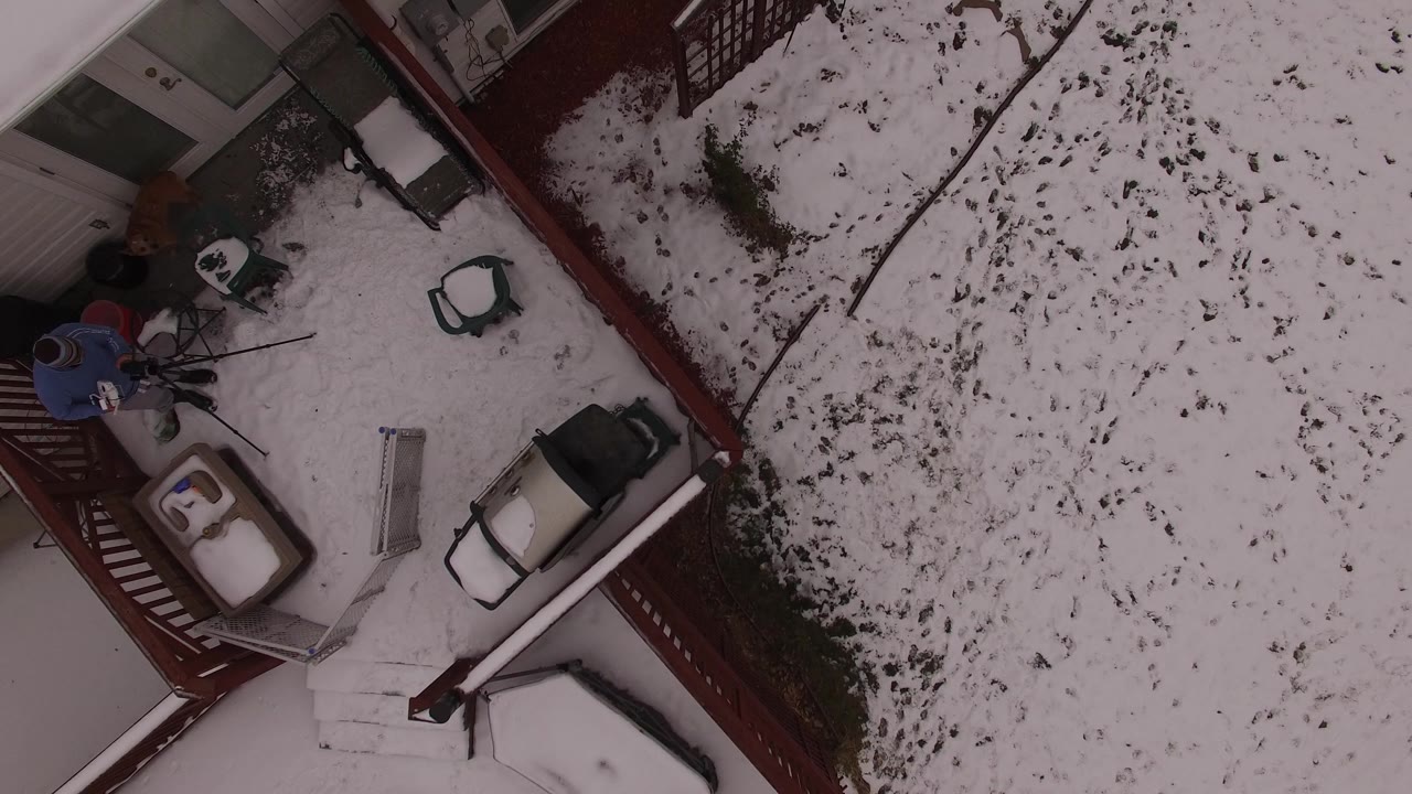 Overhead drone view in Jefferson County, Colorado shows a red-railed balcony, snow-covered yard, patio furniture, steps, and one visible person near the deck edge.