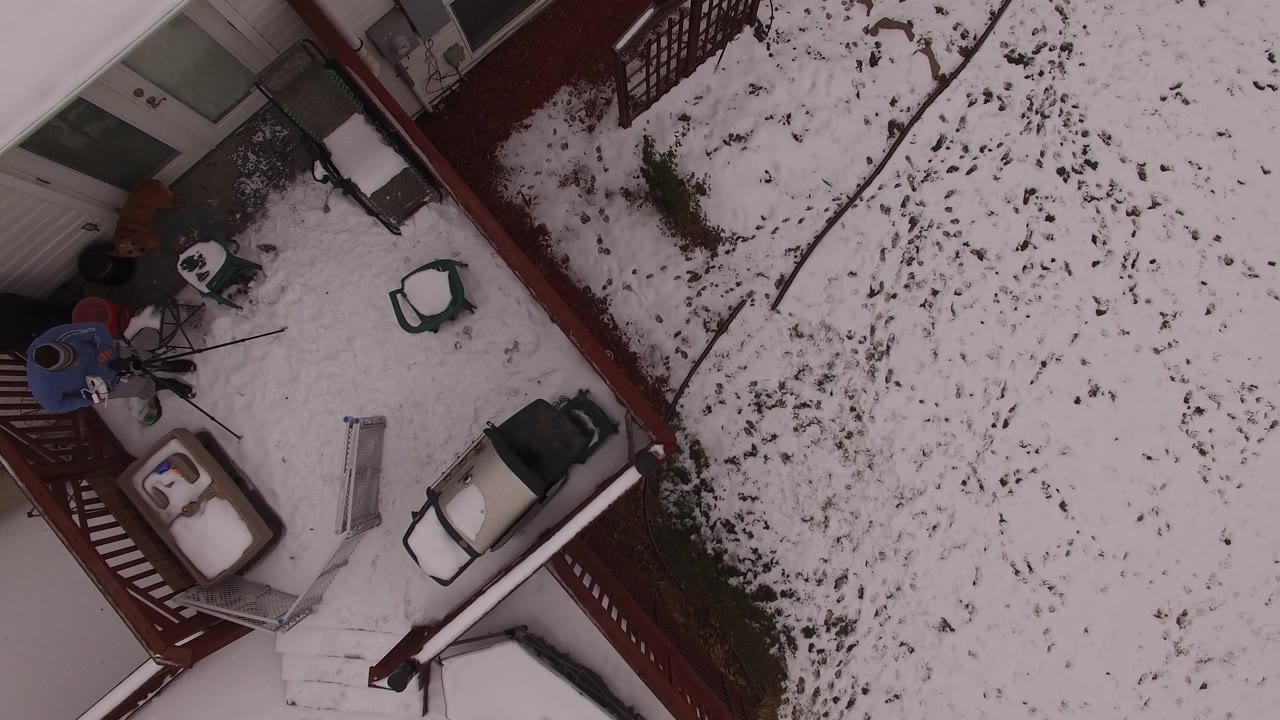 Overhead view of a snowy porch and yard beside a house.