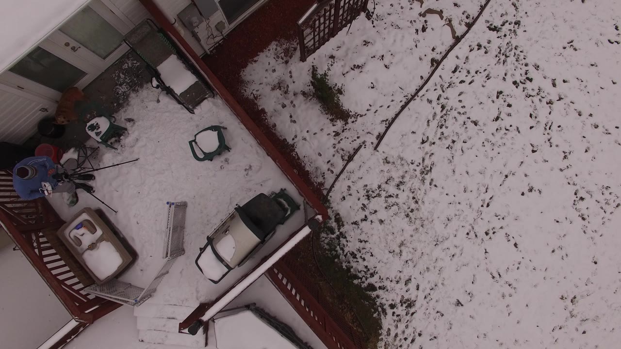 In Jefferson County, Colorado, the overhead view centers more of the porch area, with a person in a blue top standing by equipment and patio furniture on the snow-covered deck.