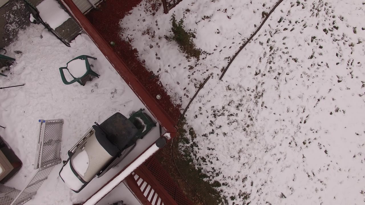 Top-down aerial view of a snowy Jefferson County, Colorado backyard with a red fence, a small pale vehicle, a metal gate, and no visible people.