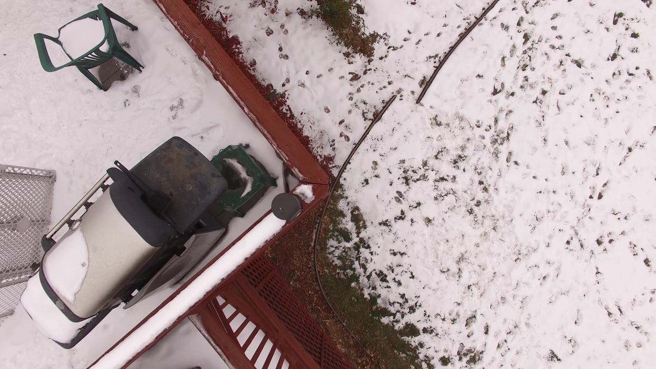 Aerial top-down view in Jefferson County, Colorado with the pale outdoor object closer to the lower left, a dark grill near the red terrace edge, scattered snow patches, and no visible people.